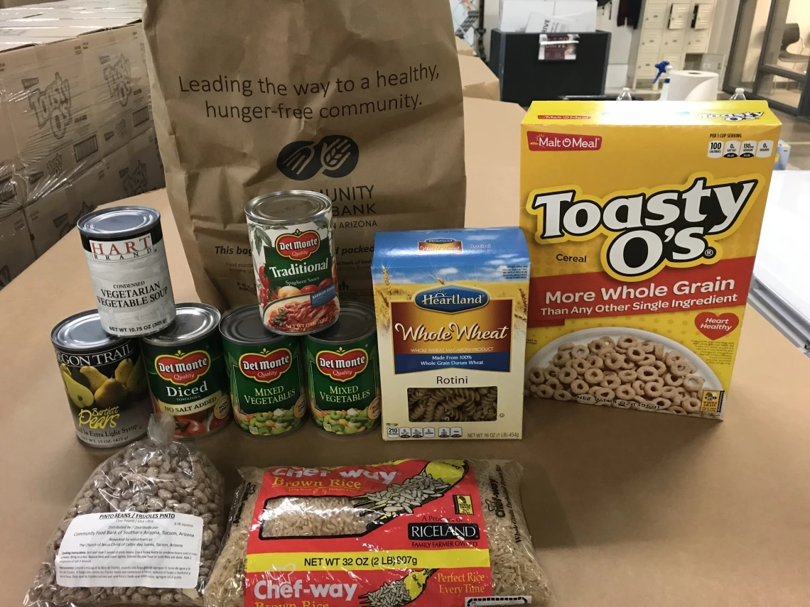 Cans of foods, whole wheat pasta, rice, beans, and cereal on a table. 