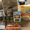 Cans of foods, whole wheat pasta, rice, beans, and cereal on a table. 