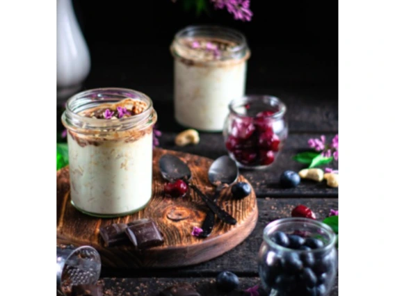 Mason jars with porridge on a black background with flowers, blueberries, mint, and shaved dark chocolate